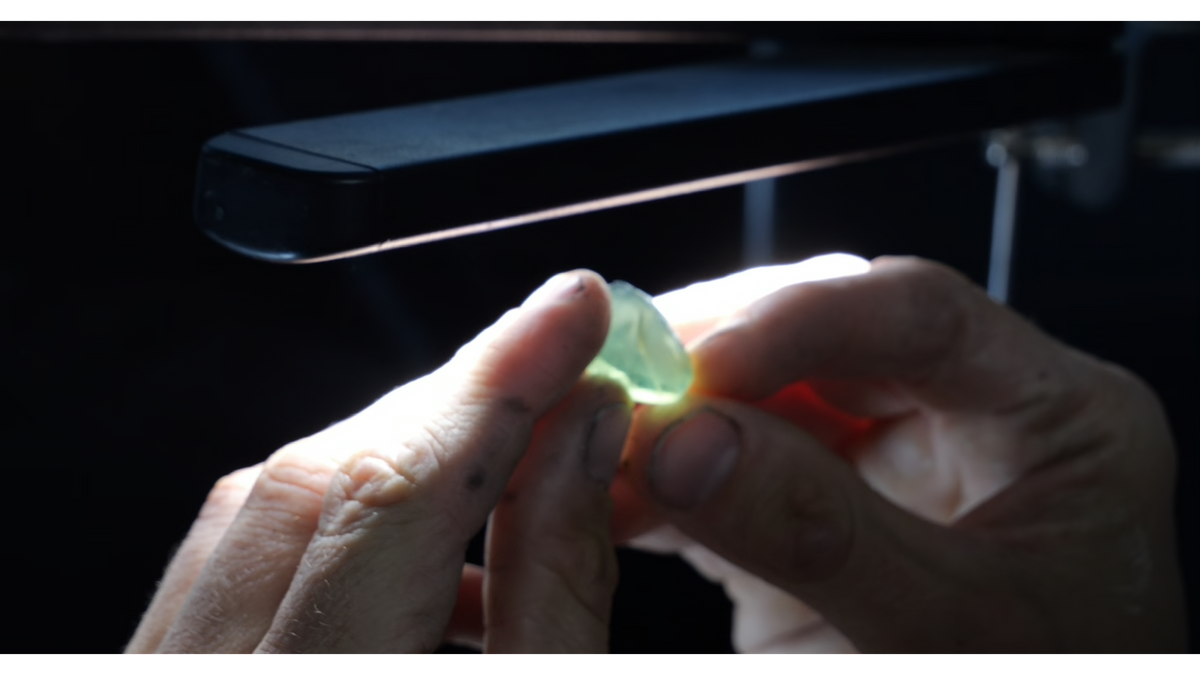 Hands holding a pale green sapphire beneath a bright inspection light before faceting.