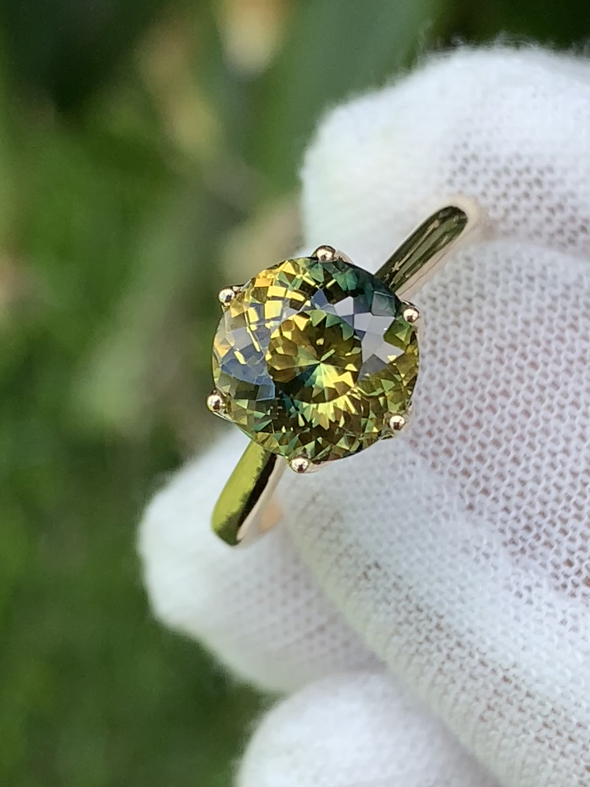 Close-up of a yellow and green parti sapphire in a claw-set solitaire ring.