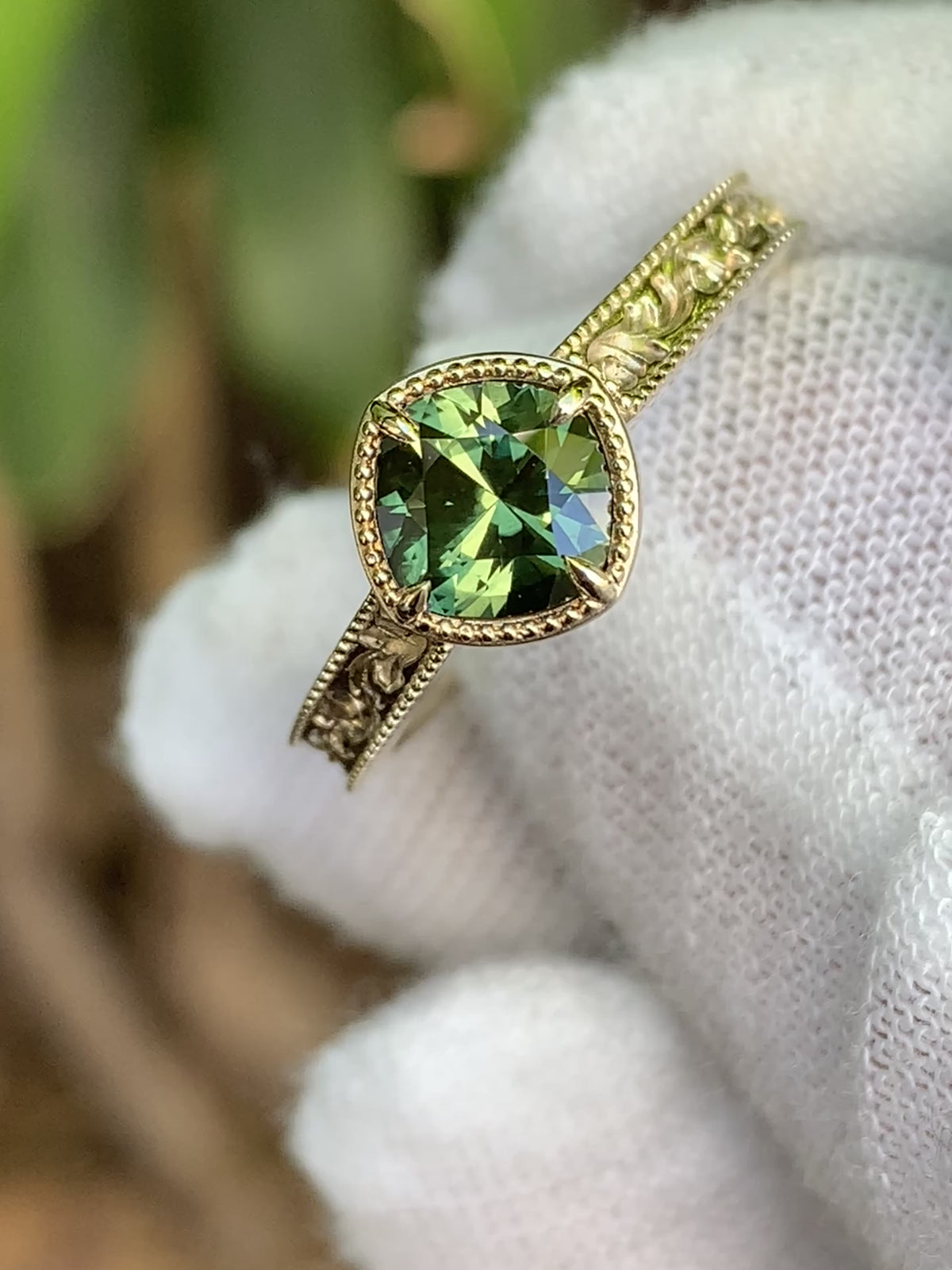 Green sapphire ring with decorative leaf detailing along the band and a fine beaded border around the centre setting.