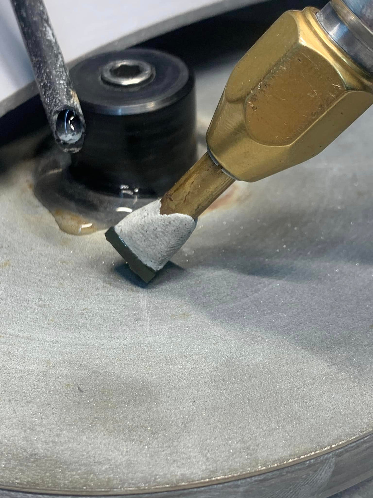 Close-up of a sapphire secured in a brass holder against a cutting disc, with a water nozzle beside it.
