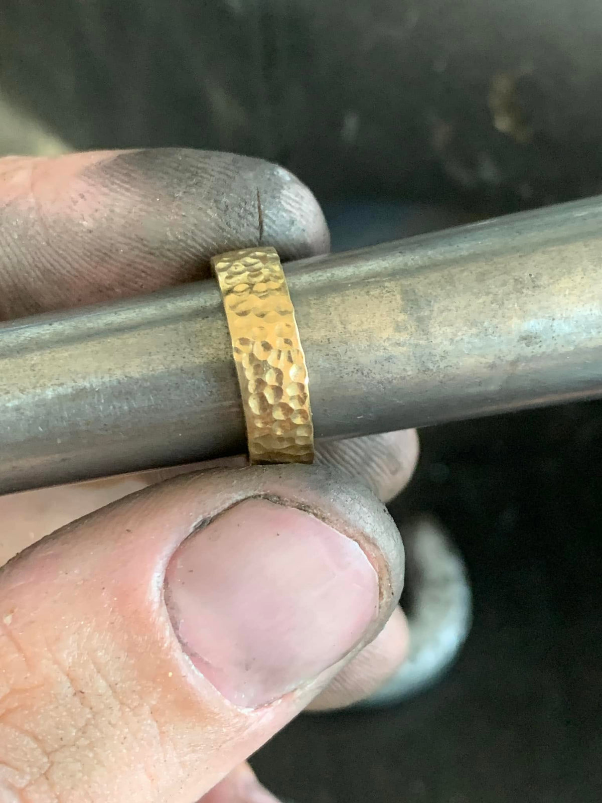 Close-up of a ring band with a hammered surface, held on a metal mandrel at the workbench.