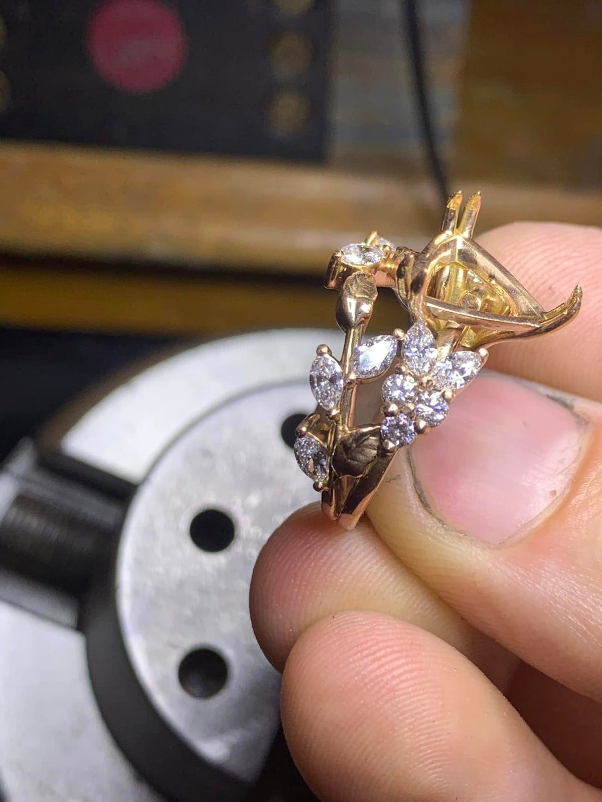 An unfinished botanical ring with leaf-shaped white accent stones and an empty centre setting, held between fingertips.