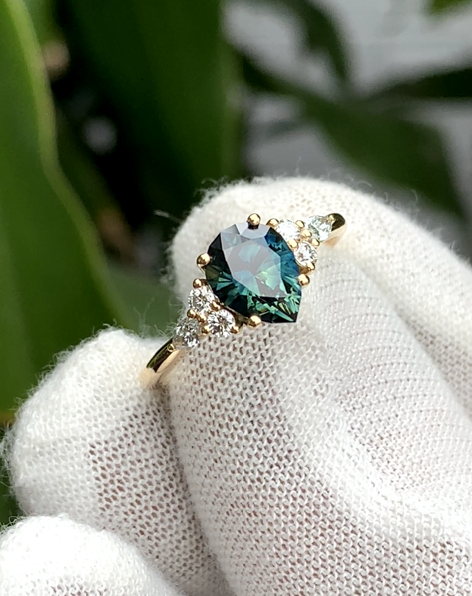 Teal sapphire ring with clusters of white accent stones on either side.