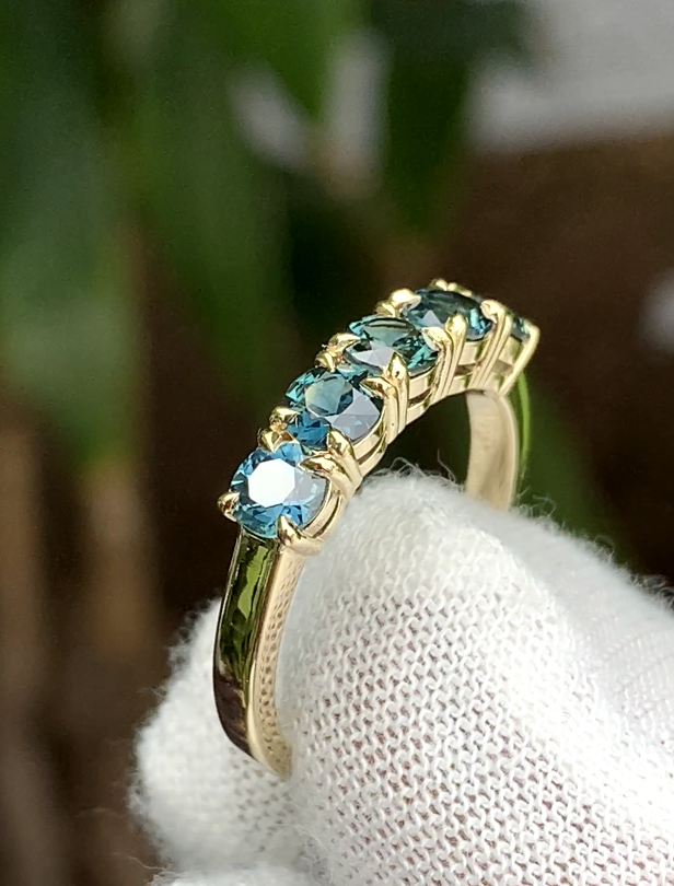 A row of round teal sapphires in claw settings across a polished band.